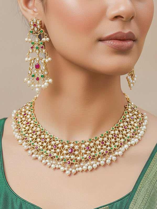 Close-up of a woman wearing an ornate traditional collar Ruby Pink and Green  jadau gold jewellery set and jadau earrings with pearls and Navratan gemstones. Bride wearing a traditional Jadau artificial necklace set for her wedding ceremony. Festive celebration look featuring a Jadau artificial necklace.