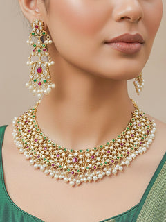 Close-up of a woman wearing an ornate traditional collar Ruby Pink and Green  jadau gold jewellery set and jadau earrings with pearls and Navratan gemstones. Bride wearing a traditional Jadau artificial necklace set for her wedding ceremony. Festive celebration look featuring a Jadau artificial necklace.