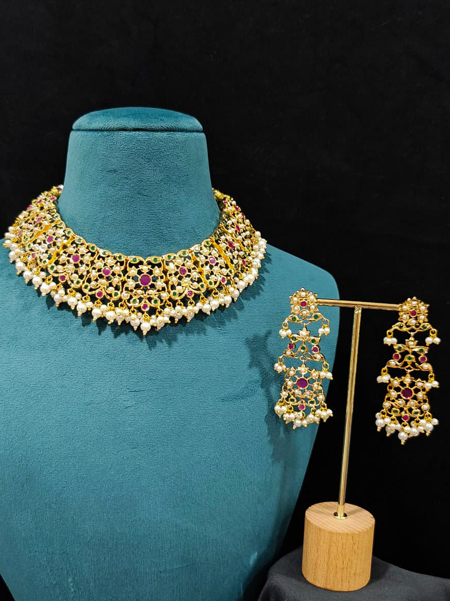 Close-up of an ornate traditional collar Ruby Pink and Green  jadau gold jewellery set and jadau earrings with pearls and Navratan gemstones. Royal Jadau necklace for festive events in India. Festive celebration look featuring a Jadau artificial necklace.