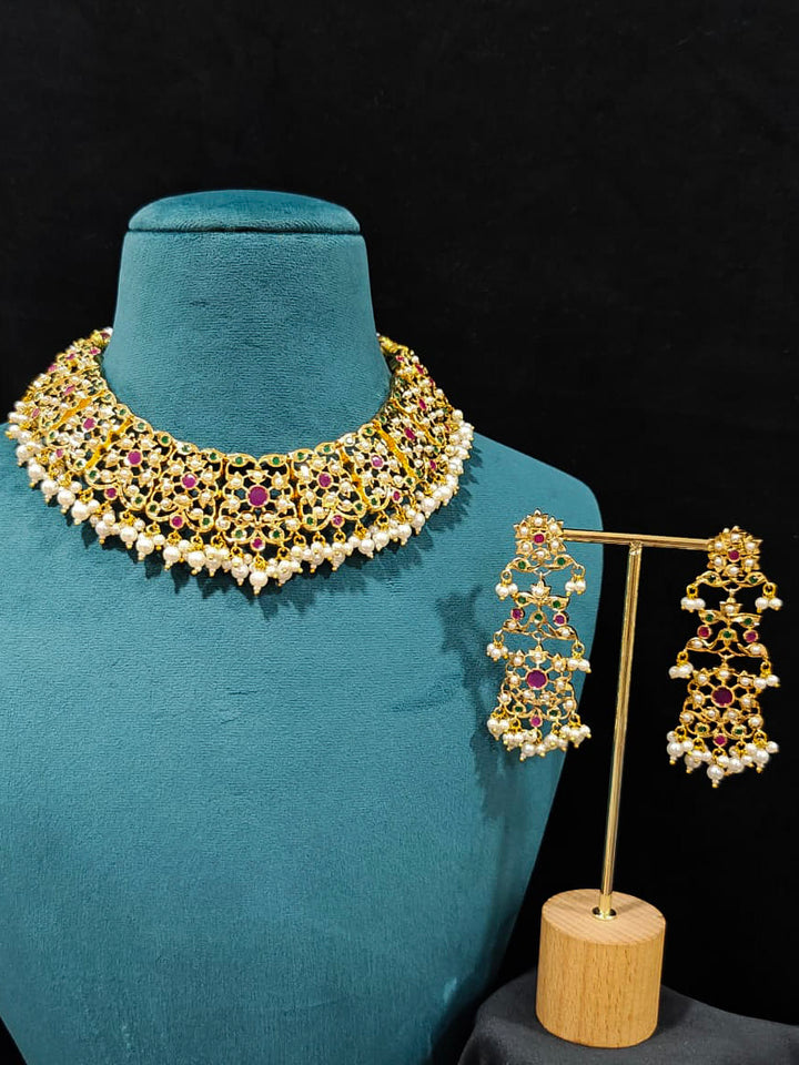 Close-up of an ornate traditional collar Ruby Pink and Green  jadau gold jewellery set and jadau earrings with pearls and Navratan gemstones. Royal Jadau necklace for festive events in India. Festive celebration look featuring a Jadau artificial necklace.