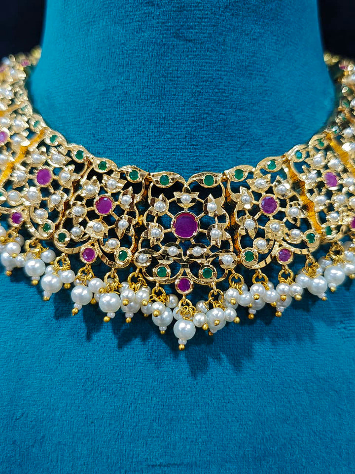 Close-up of an ornate traditional collar Ruby Pink and Green  jadau gold jewellery set and jadau earrings with pearls and Navratan gemstones. Royal Jadau necklace for festive events in India. Festive celebration look featuring a Jadau artificial necklace.