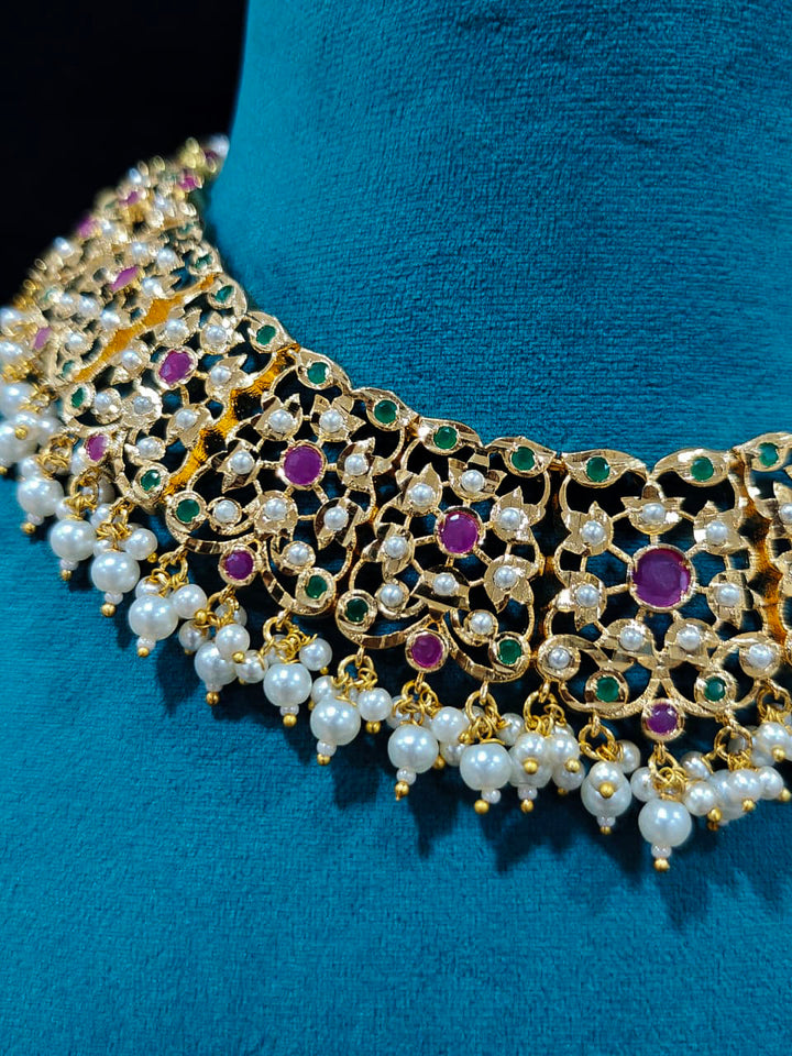 Close-up of an ornate traditional collar Ruby Pink and Green  jadau gold jewellery set and jadau earrings with pearls and Navratan gemstones. Royal Jadau necklace for festive events in India. Festive celebration look featuring a Jadau artificial necklace.