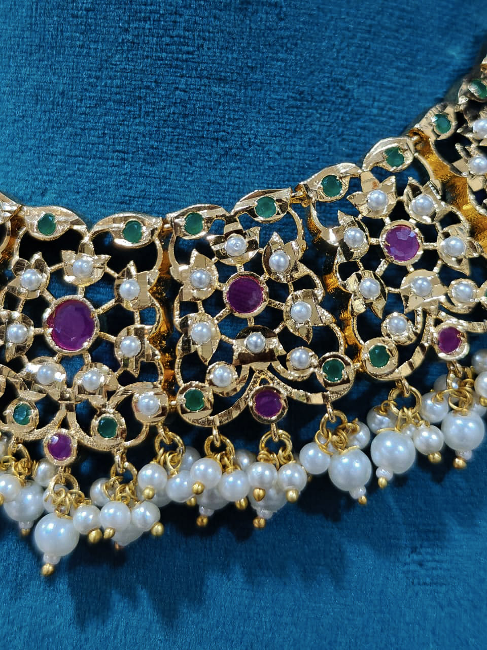 Close-up of an ornate traditional collar Ruby Pink and Green  jadau gold jewellery set and jadau earrings with pearls and Navratan gemstones. Royal Jadau necklace for festive events in India. Festive celebration look featuring a Jadau artificial necklace.