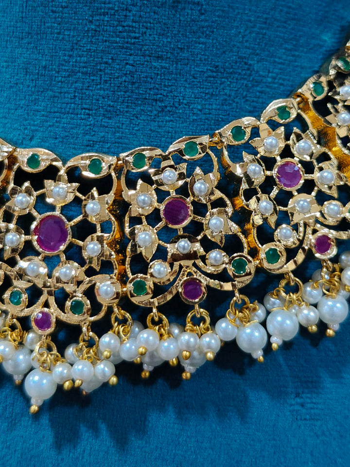 Close-up of an ornate traditional collar Ruby Pink and Green  jadau gold jewellery set and jadau earrings with pearls and Navratan gemstones. Royal Jadau necklace for festive events in India. Festive celebration look featuring a Jadau artificial necklace.