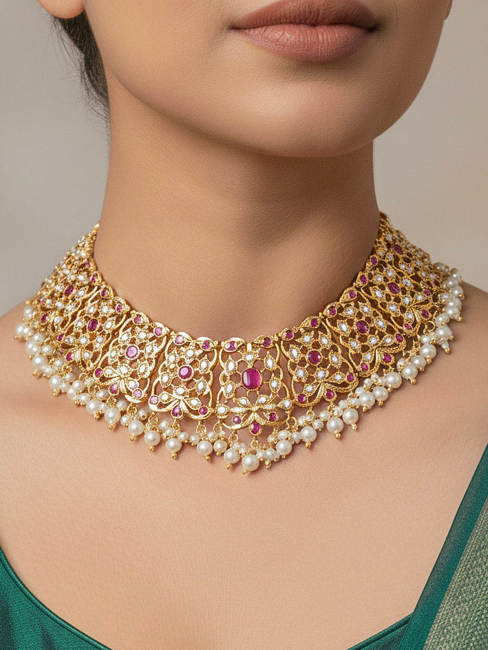 Close-up of a woman wearing an ornate traditional Ruby Pink jadau gold jewellery set and jadau earrings with pearls and stones. Perfect Jadau necklace set for weddings and festivals. Woman pairing a traditional Jadau necklace with a silk saree.