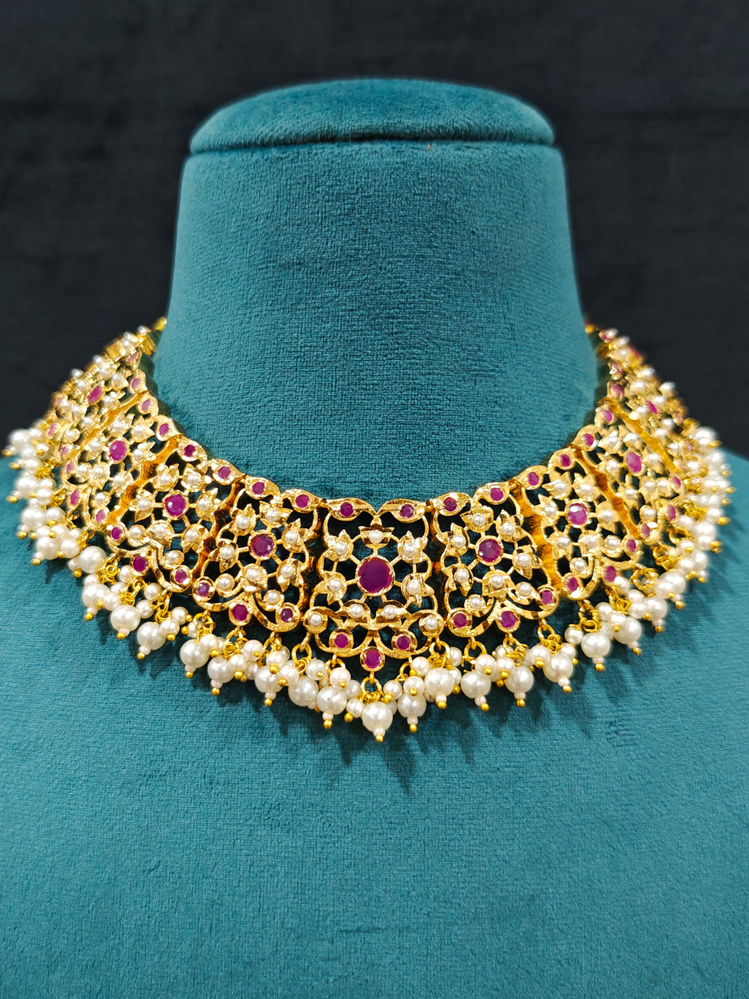 Close-up of an ornate traditional Ruby Pink jadau gold jewellery set and jadau earrings with pearls and stones. Elegant reception look featuring a luxury Jadau artificial jewelry set. Perfect Jadau necklace set for weddings and festivals. 