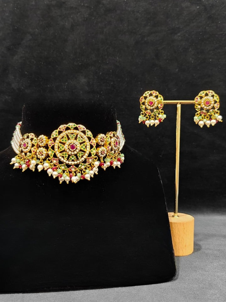 Close-up of an ornate traditional Choker jadau gold jewellery set and  jadau earrings with Pearl, Beads, and Pink & Green Colored Stone. Wedding guest styling a statement Jadau artificial necklace. A royal Jadau necklace for festive events in India.