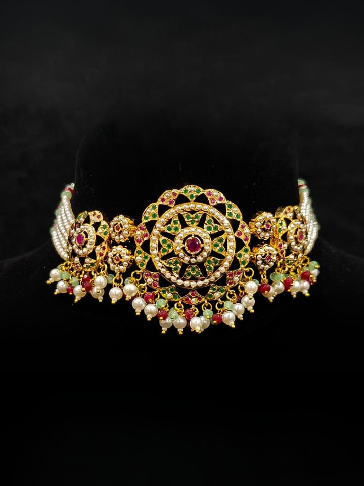 Close-up of an ornate traditional Choker jadau gold jewellery set and  jadau earrings with Pearl, Beads, and Pink & Green Colored Stone. Wedding guest styling a statement Jadau artificial necklace. A royal Jadau necklace for festive events in India.