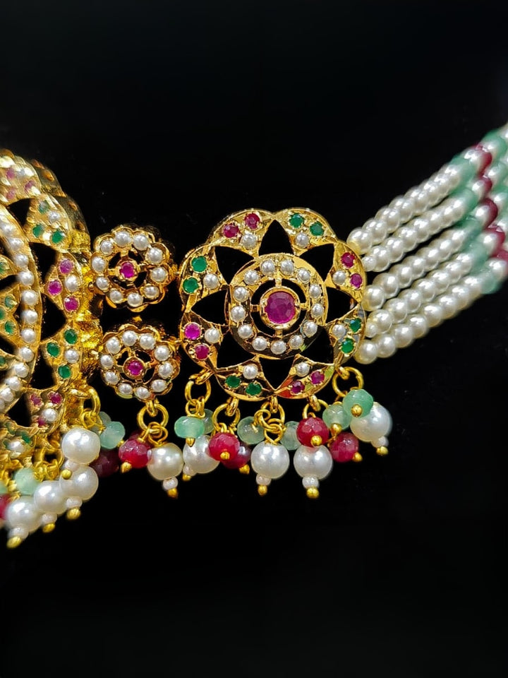 Close-up of an ornate traditional Choker jadau gold jewellery set and  jadau earrings with Pearl, Beads, and Pink & Green Colored Stone. Wedding guest styling a statement Jadau artificial necklace. A royal Jadau necklace for festive events in India.
