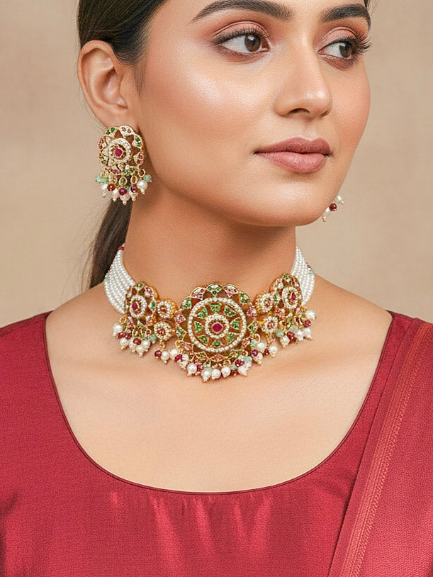 Close-up of a woman wearing an ornate traditional Choker jadau gold jewellery set and  jadau earrings with Pearl, Beads, and Pink and Green Colored Stone. Woman wearing a royal Jadau necklace for festive events in India. Festive saree, Lehenga and Anarkali look completed with a Jadau necklace.