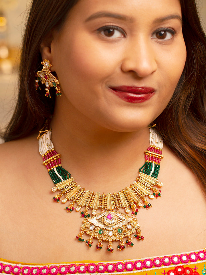 A woman smiles softly wearing the Svarlina Green & Pink Necklace Set, featuring a Kundan necklace with green and red crystal stones, matching earrings, and a gold-embroidered pink traditional outfit—ideal elegant party wear jewelry.