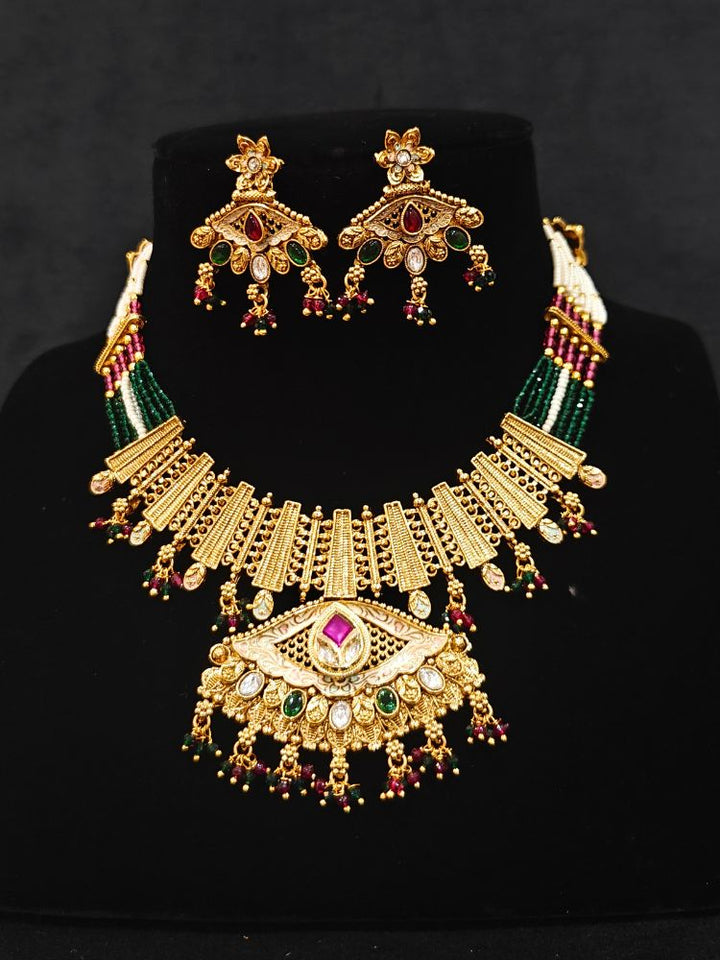 Close-up of an ornate traditional (Gold Polish) Pink & Green Collar jewellery set and earrings with Crystal Beads, Meenakari, Pearl and Colored Stone. Bride wearing a high-quality artificial Meenakari jewelry set for wedding rituals. Woman wearing lightweight artificial Meenakari jewelry for long wedding functions.