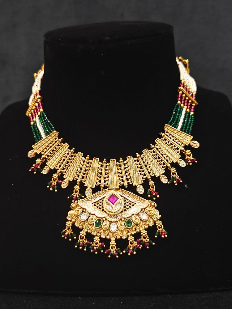 Close-up of a woman wearing an ornate traditional (Gold Polish) Pink & Green Collar jewellery set and earrings with Crystal Beads, Meenakari, Pearl and Colored Stone. Bride wearing a high-quality artificial Meenakari jewelry set for wedding rituals. Woman wearing lightweight artificial Meenakari jewelry for long wedding functions.