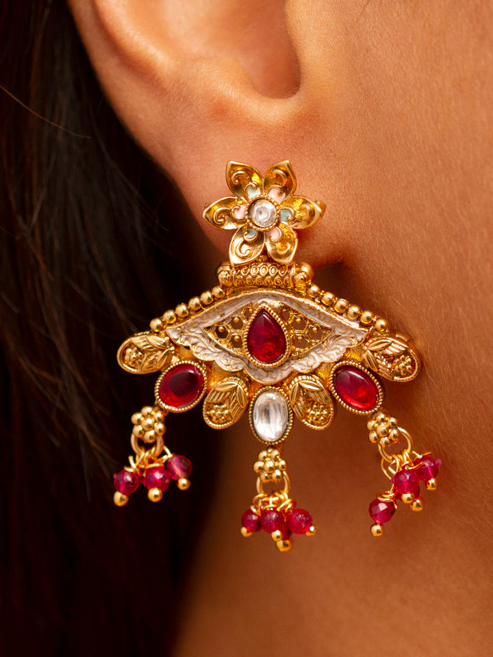 A woman smiles softly wearing the Svarlina Pink Necklace Set, featuring a Kundan necklace with red crystal stones, matching earrings, and a gold-embroidered pink traditional outfit—ideal elegant party wear jewelry.