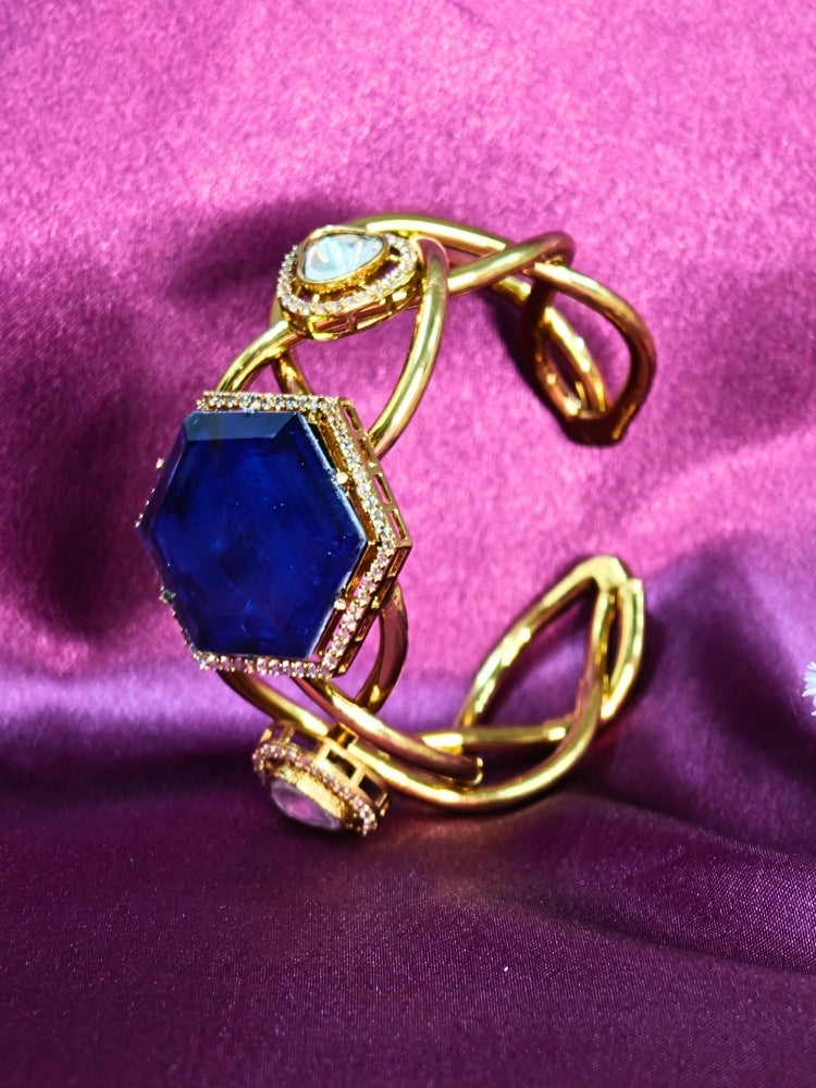 The Tahira Navy Blue Bracelet (Adjustable) features a large hexagonal Navy Blue stone at the center, with an american diamond border and two round kundan stones on each side, displayed on purple satin fabric with white flowers in the background.