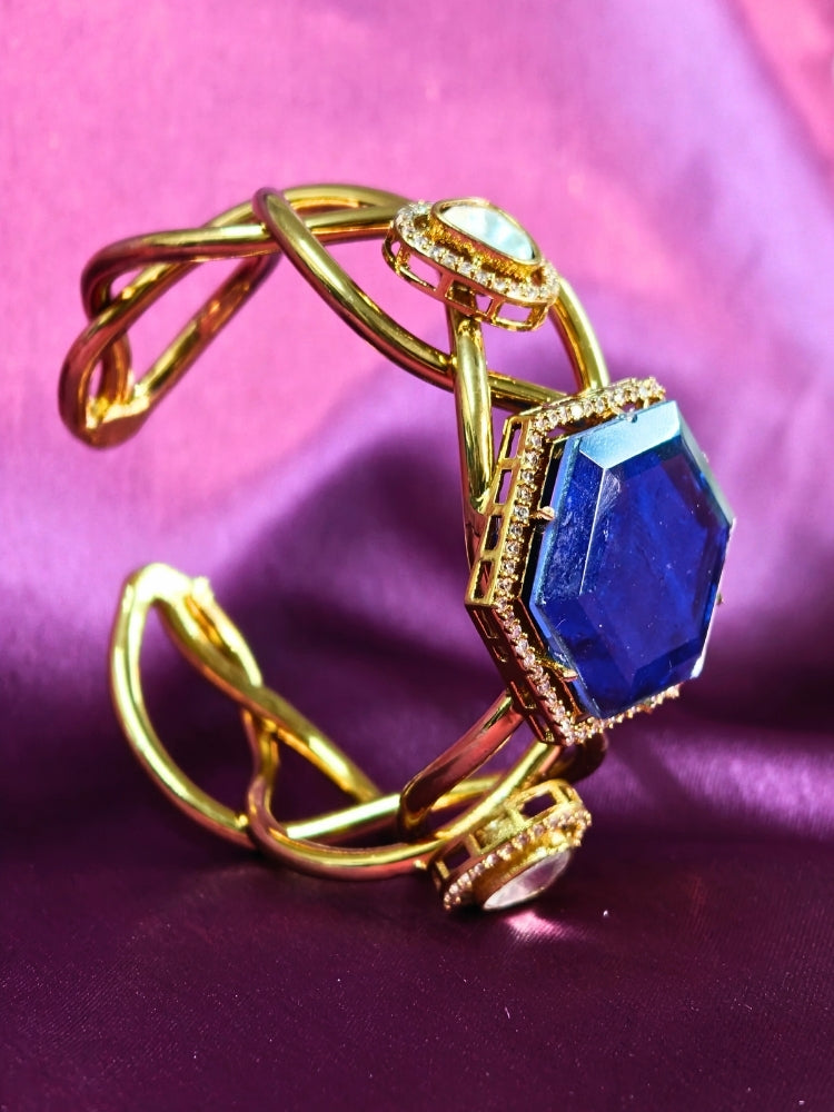 The Tahira Navy Blue Bracelet (Adjustable) features a large hexagonal Navy Blue stone at the center, with an american diamond border and two round kundan stones on each side, displayed on purple satin fabric with white flowers in the background.