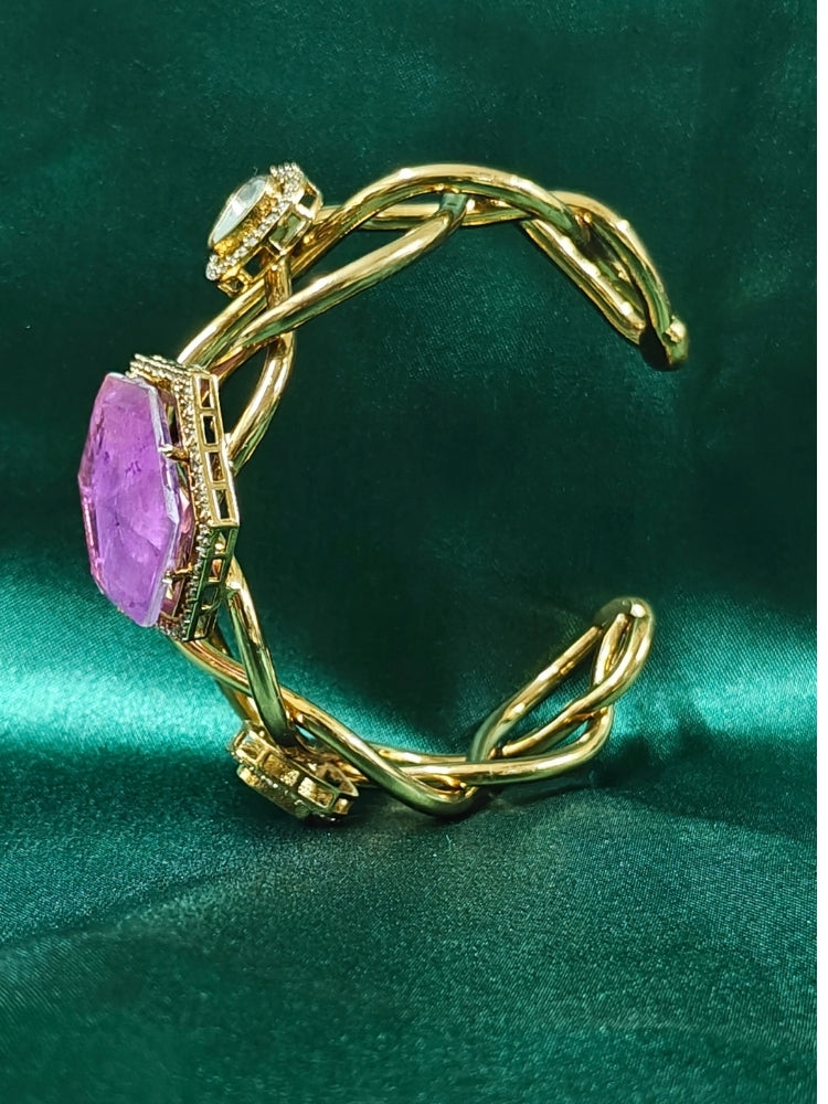 The Tahira Purple Bracelet (Adjustable) features a large hexagonal Purple stone at the center, with an american diamond border and two round kundan stones on each side, displayed on Green satin fabric with white flowers in the background.