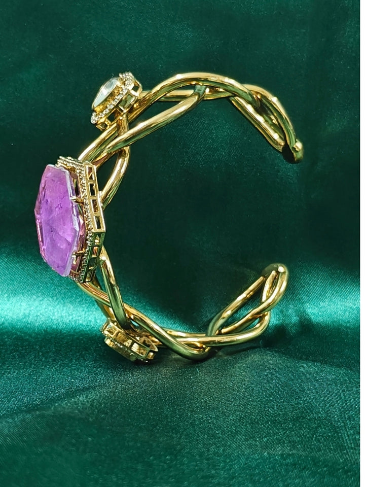 The Tahira Purple Bracelet (Adjustable) features a large hexagonal Purple stone at the center, with an american diamond border and two round kundan stones on each side, displayed on Green satin fabric with white flowers in the background.
