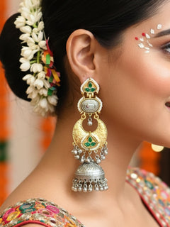A close-up of a womans ear wearing Tapasya Green Earrings, ornate gold and silver with floral designs, colored stones, dangling silver beads, and a large intricate jhumka dome at the bottom. Long Oxidized earrings, german silver earrings, navratri earrings.  Jhumka earrings. Jhumki Earrings. 