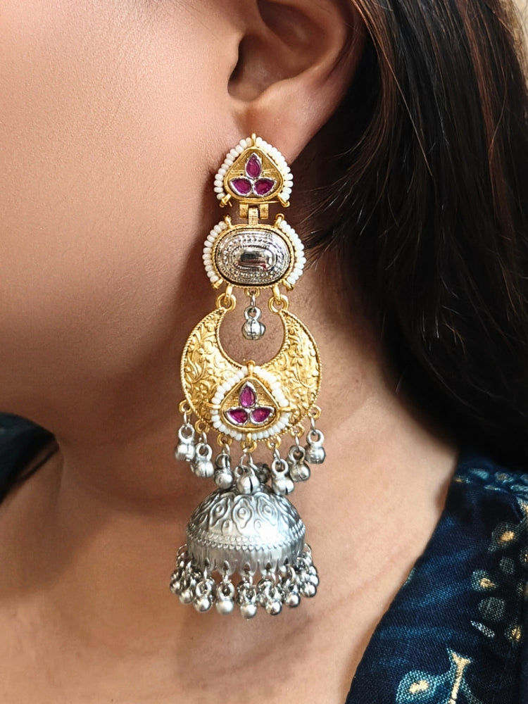 A close-up of a womans ear wearing Tapasya Pink Earrings, ornate gold and silver with floral designs, colored stones, dangling silver beads, and a large intricate jhumka dome at the bottom. Long Oxidized earrings, german silver earrings, navratri earrings.  Jhumka earrings. Jhumki Earrings. 