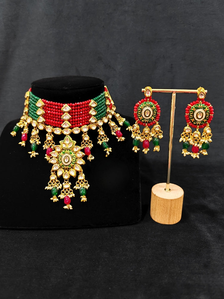 Close-up of an ornate traditional Red and Green Meenakari gold Choker jewellery set and earrings with Kundan, Meenakari Work, Red & Green Crystal Beads, Pearls and Red & Green Tumble Stone. Saree look completed with an elegant Meenakari artificial jewelry piece. Perfect Meenakari necklace set for weddings and festivals.
