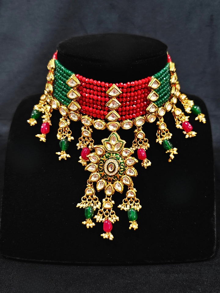 Close-up of an ornate traditional Red and Green Meenakari gold Choker jewellery set and earrings with Kundan, Meenakari Work, Red & Green Crystal Beads, Pearls and Red & Green Tumble Stone. Saree look completed with an elegant Meenakari artificial jewelry piece. Perfect Meenakari necklace set for weddings and festivals.