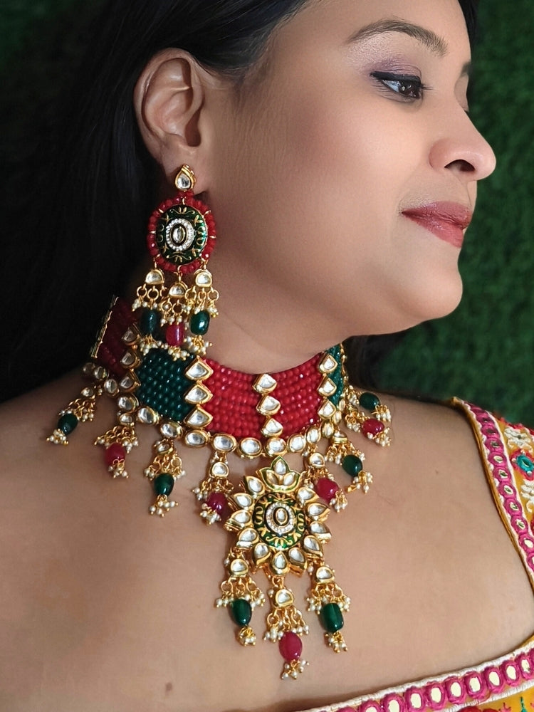 Close-up of a woman wearing an ornate traditional Red and Green Meenakari gold Choker jewellery set and earrings with Kundan, Meenakari Work, Red & Green Crystal Beads, Pearls and Red & Green Tumble Stone. Woman wearing a vibrant Meenakari artificial jewelry set for celebrations. Saree look completed with an elegant Meenakari artificial jewelry piece.