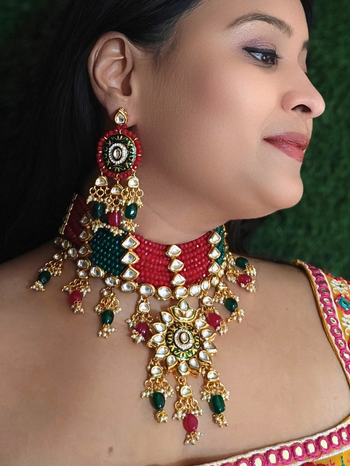 Close-up of a woman wearing an ornate traditional Red and Green Meenakari gold Choker jewellery set and earrings with Kundan, Meenakari Work, Red & Green Crystal Beads, Pearls and Red & Green Tumble Stone. Woman wearing a vibrant Meenakari artificial jewelry set for celebrations. Saree look completed with an elegant Meenakari artificial jewelry piece.