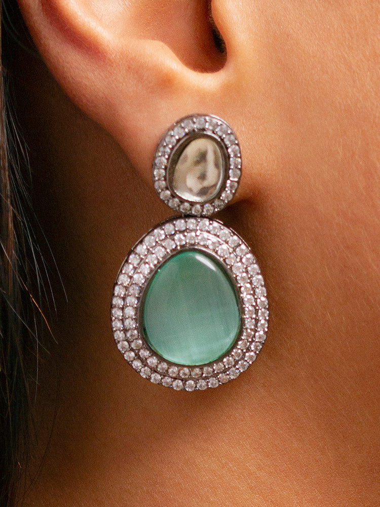 A woman with brown hair down smiles to the side, wearing the Teel Green Elizabeth Necklace Set featuring a statement Victorian-style necklace and matching earrings with large colorful stones, paired with a sparkly dark top.