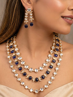 Close-up of a woman wearing an ornate traditional (Gold Polish) Navy Blue Layered jewellery set and earrings with Polki and Navy Blue Colored Stones. Wedding guest wearing a statement Polki artificial necklace for a reception party. Woman styling a premium Polki imitation necklace for wedding celebrations.