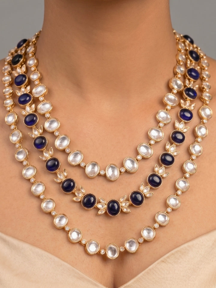 Close-up of a woman wearing an ornate traditional (Gold Polish) Navy Blue Layered jewellery set and earrings with Polki and Navy Blue Colored Stones. Wedding guest wearing a statement Polki artificial necklace for a reception party. Woman styling a premium Polki imitation necklace for wedding celebrations.