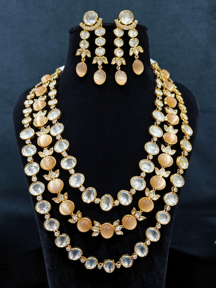 Close-up of an ornate traditional (Gold Polish) Peach Layered jewellery set and earrings with Polki and Peach Colored Stones. Wedding guest wearing a statement Polki artificial necklace for a reception party. Woman styling a premium Polki imitation necklace for wedding celebrations.