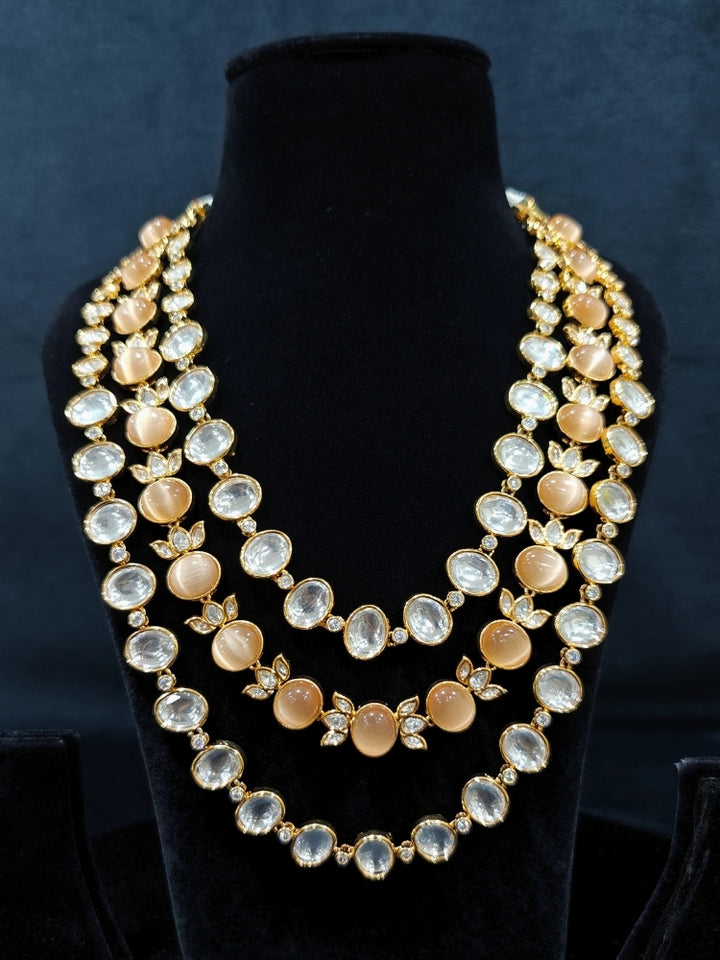 Close-up of an ornate traditional (Gold Polish) Peach Layered jewellery set and earrings with Polki and Peach Colored Stones. Wedding guest wearing a statement Polki artificial necklace for a reception party. Woman styling a premium Polki imitation necklace for wedding celebrations.
