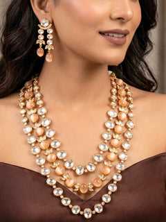Close-up of a woman wearing an ornate traditional (Gold Polish) Peach Layered jewellery set and earrings with Polki and Peach Colored Stones. Wedding guest wearing a statement Polki artificial necklace for a reception party. Woman styling a premium Polki imitation necklace for wedding celebrations.