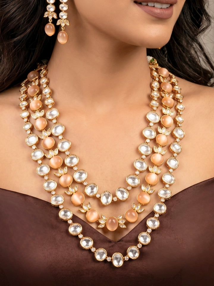 Close-up of a woman wearing an ornate traditional (Gold Polish) Peach Layered jewellery set and earrings with Polki and Peach Colored Stones. Wedding guest wearing a statement Polki artificial necklace for a reception party. Woman styling a premium Polki imitation necklace for wedding celebrations.
