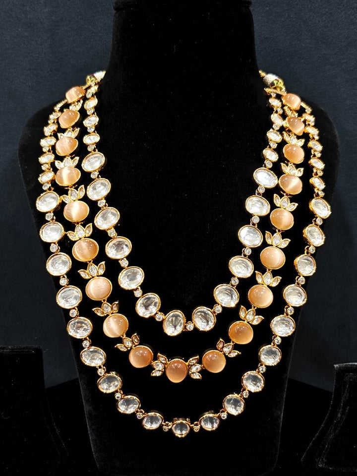 Close-up of an ornate traditional (Gold Polish) Peach Layered jewellery set and earrings with Polki and Peach Colored Stones. Wedding guest wearing a statement Polki artificial necklace for a reception party. Woman styling a premium Polki imitation necklace for wedding celebrations.