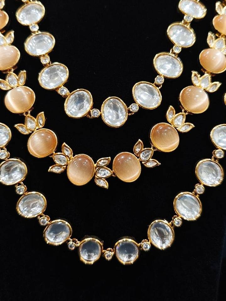 Close-up of an ornate traditional (Gold Polish) Peach Layered jewellery set and earrings with Polki and Peach Colored Stones. Wedding guest wearing a statement Polki artificial necklace for a reception party. Woman styling a premium Polki imitation necklace for wedding celebrations.