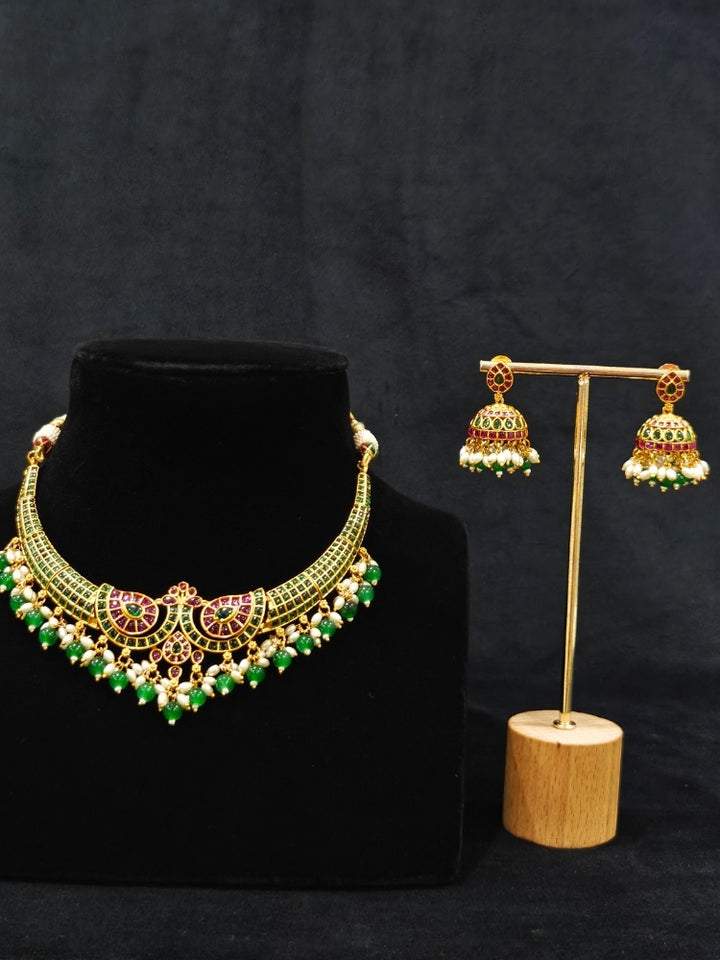 Close-up of an ornate traditional (Gold Polish) Green Collar jewellery set and earrings with Green & Pink Colored Stones, Green Beads and Pearls. Mehendi ceremony look completed with a handcrafted Colored Stones jewelry set. Saree look completed with an elegant Colored Stones artificial jewelry piece.