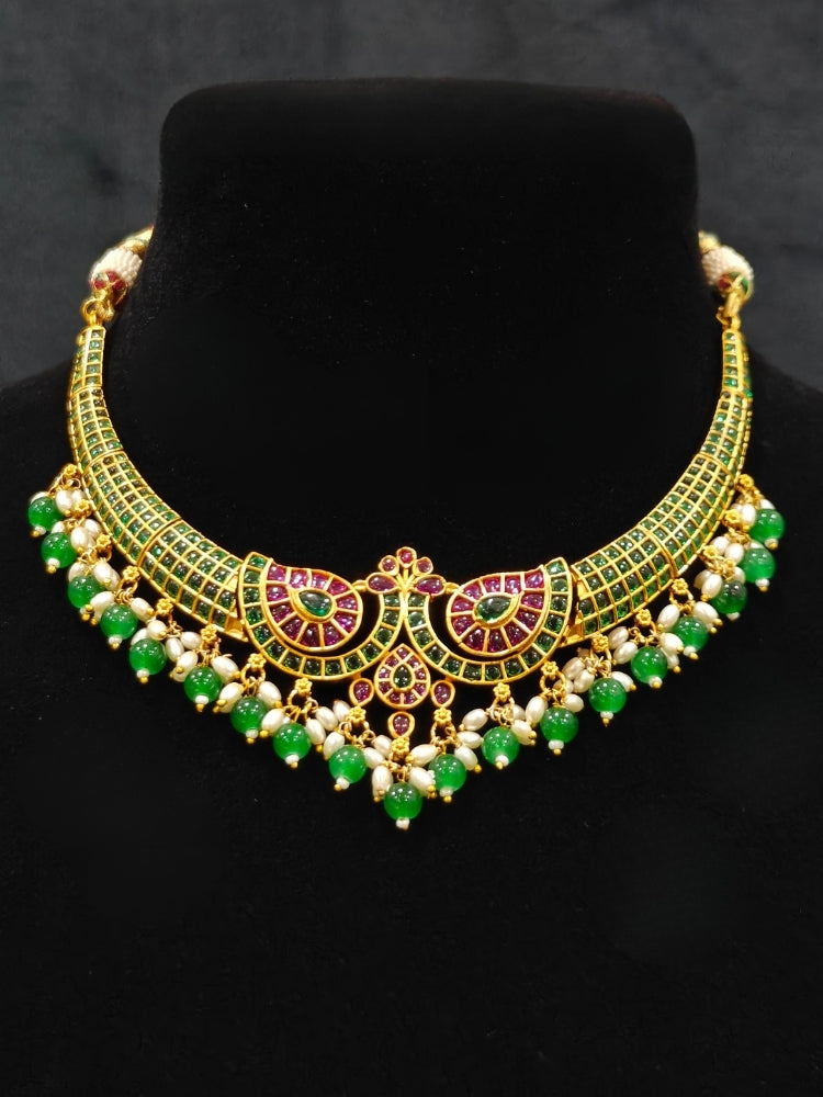 Close-up of an ornate traditional (Gold Polish) Green Collar jewellery set and earrings with Green & Pink Colored Stones, Green Beads and Pearls. Mehendi ceremony look completed with a handcrafted Colored Stones jewelry set. Saree look completed with an elegant Colored Stones artificial jewelry piece.