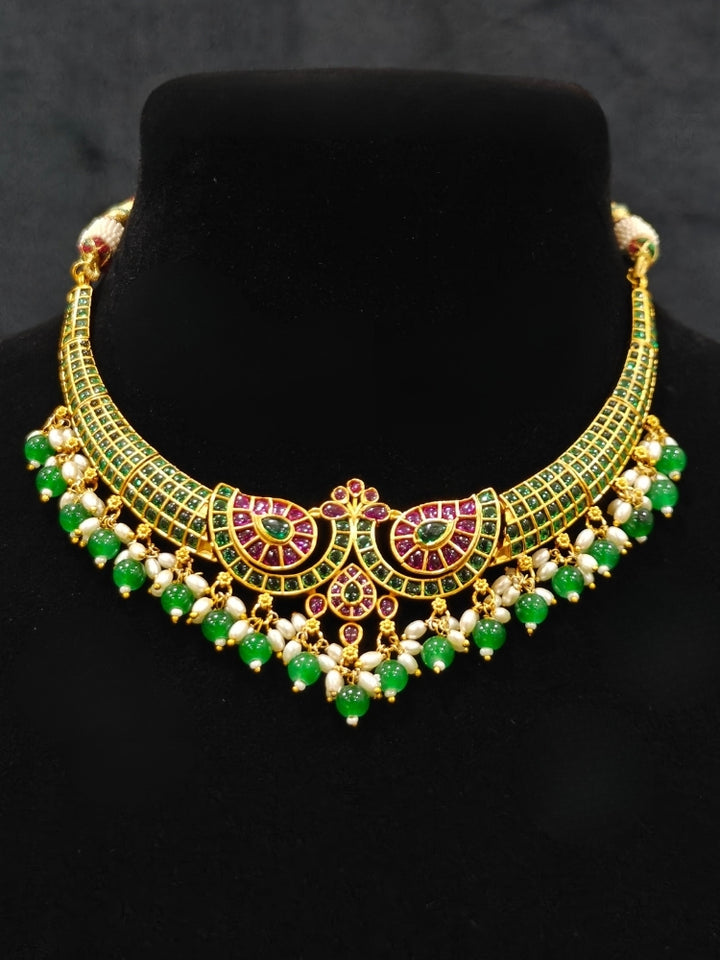 Close-up of an ornate traditional (Gold Polish) Green Collar jewellery set and earrings with Green & Pink Colored Stones, Green Beads and Pearls. Mehendi ceremony look completed with a handcrafted Colored Stones jewelry set. Saree look completed with an elegant Colored Stones artificial jewelry piece.