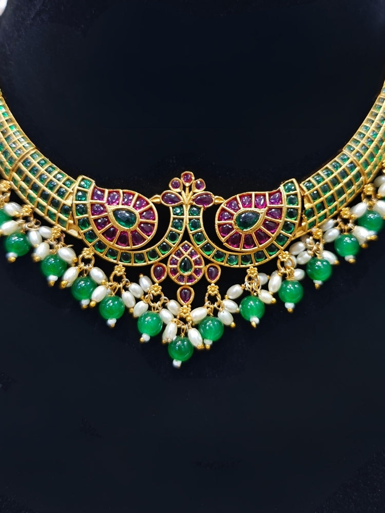 Close-up of an ornate traditional (Gold Polish) Green Collar jewellery set and earrings with Green & Pink Colored Stones, Green Beads and Pearls. Mehendi ceremony look completed with a handcrafted Colored Stones jewelry set. Saree look completed with an elegant Colored Stones artificial jewelry piece.