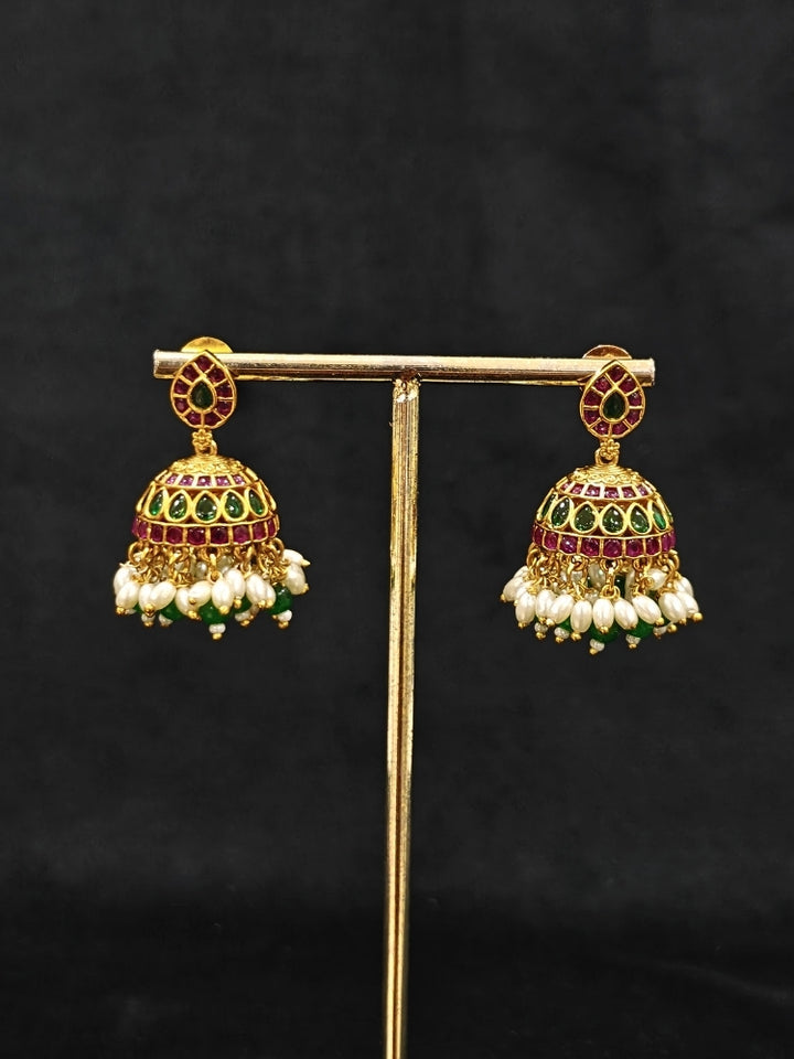 Close-up of an ornate traditional (Gold Polish) Green Collar jewellery set and earrings with Green & Pink Colored Stones, Green Beads and Pearls. Mehendi ceremony look completed with a handcrafted Colored Stones jewelry set. Saree look completed with an elegant Colored Stones artificial jewelry piece.