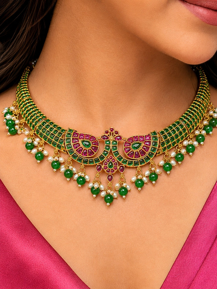 Close-up of a women wearing an ornate traditional (Gold Polish) Green Collar jewellery set and earrings with Green & Pink Colored Stones, Green Beads and Pearls. Mehendi ceremony look completed with a handcrafted Colored Stones jewelry set. Saree look completed with an elegant Colored Stones artificial jewelry piece.