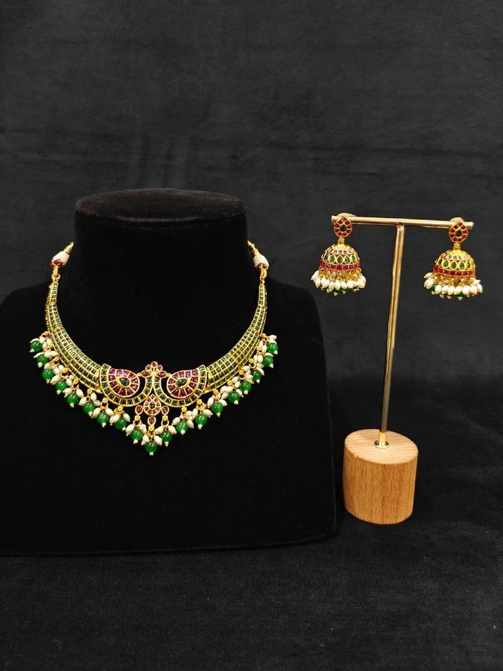 Close-up of an ornate traditional (Gold Polish) Green Collar jewellery set and earrings with Green & Pink Colored Stones, Green Beads and Pearls. Mehendi ceremony look completed with a handcrafted Colored Stones jewelry set. Saree look completed with an elegant Colored Stones artificial jewelry piece.