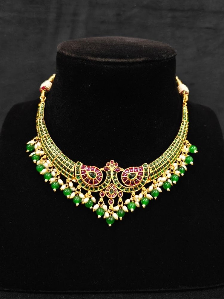 Close-up of an ornate traditional (Gold Polish) Green Collar jewellery set and earrings with Green & Pink Colored Stones, Green Beads and Pearls. Mehendi ceremony look completed with a handcrafted Colored Stones jewelry set. Saree look completed with an elegant Colored Stones artificial jewelry piece.