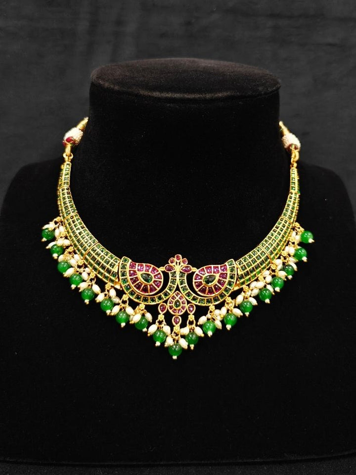 Close-up of an ornate traditional (Gold Polish) Green Collar jewellery set and earrings with Green & Pink Colored Stones, Green Beads and Pearls. Mehendi ceremony look completed with a handcrafted Colored Stones jewelry set. Saree look completed with an elegant Colored Stones artificial jewelry piece.