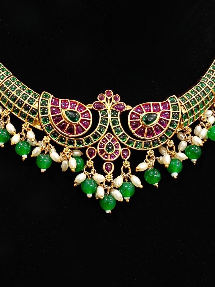 Close-up of an ornate traditional (Gold Polish) Green Collar jewellery set and earrings with Green & Pink Colored Stones, Green Beads and Pearls. Mehendi ceremony look completed with a handcrafted Colored Stones jewelry set. Saree look completed with an elegant Colored Stones artificial jewelry piece.