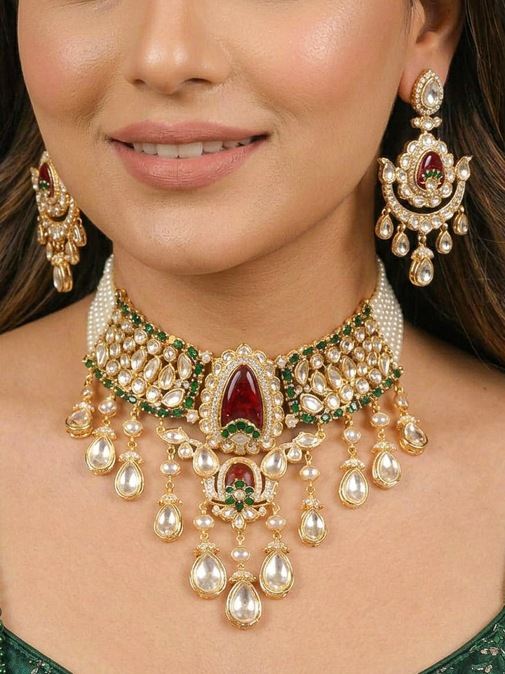 Close-up of a woman wearing an ornate traditional (Bright Gold) Red and Green Choker jewellery set and earrings and maangtikka with Uncut Kundan, American Diamond, Green Colored Stones, Pearls and Doublet Stone. Bride showcasing a premium imitation Moissanite jewelry set for her reception look. Wedding celebration styling with a luxury artificial Moissanite jewelry Set design.
