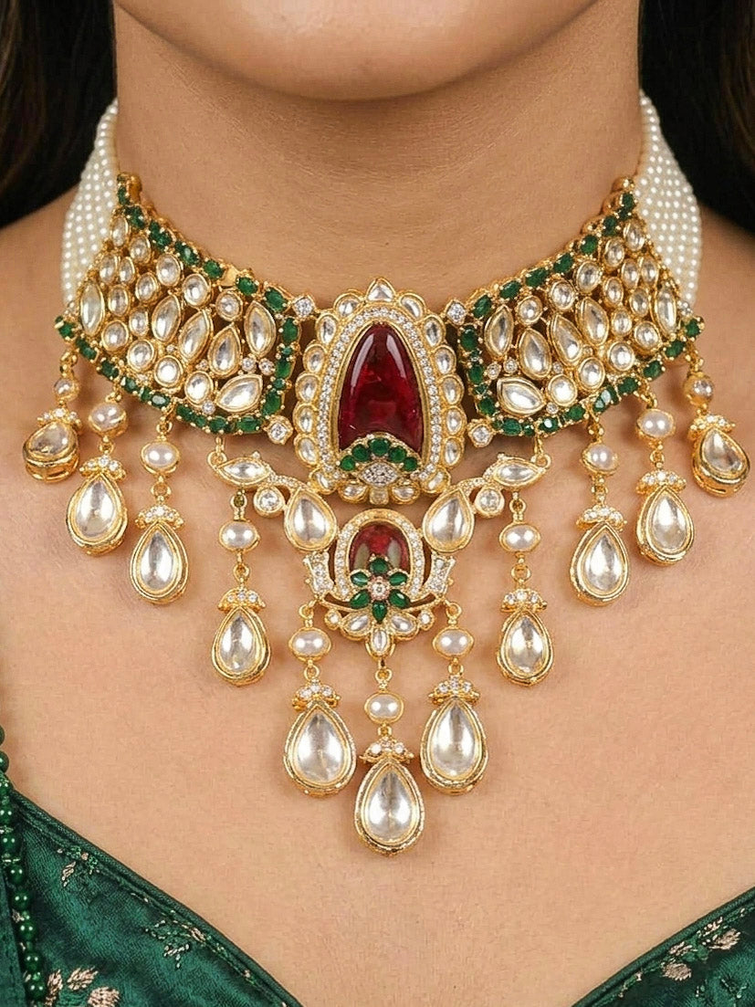 Close-up of a woman wearing an ornate traditional (Bright Gold) Red and Green Choker jewellery set and earrings and maangtikka with Uncut Kundan, American Diamond, Green Colored Stones, Pearls and Doublet Stone. Bride showcasing a premium imitation Moissanite jewelry set for her reception look. Wedding celebration styling with a luxury artificial Moissanite jewelry Set design.