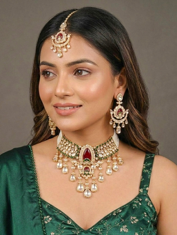 Close-up of a woman wearing an ornate traditional (Bright Gold) Red and Green Choker jewellery set and earrings and maangtikka with Uncut Kundan, American Diamond, Green Colored Stones, Pearls and Doublet Stone. Bride showcasing a premium imitation Moissanite jewelry set for her reception look. Wedding celebration styling with a luxury artificial Moissanite jewelry Set design.